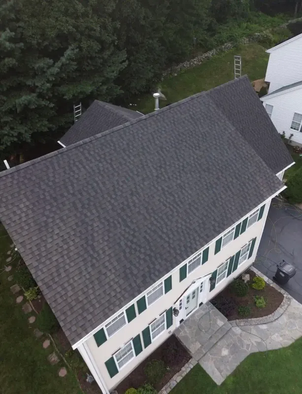 Aerial view of a white two-story home with a new shingle roof and green shutters
